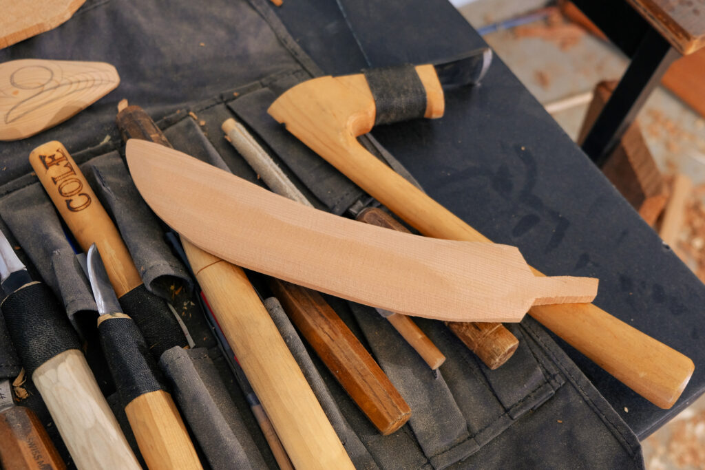 Wood carving tools including chisels, knives, and unfinished wooden shapes on a dark cloth.