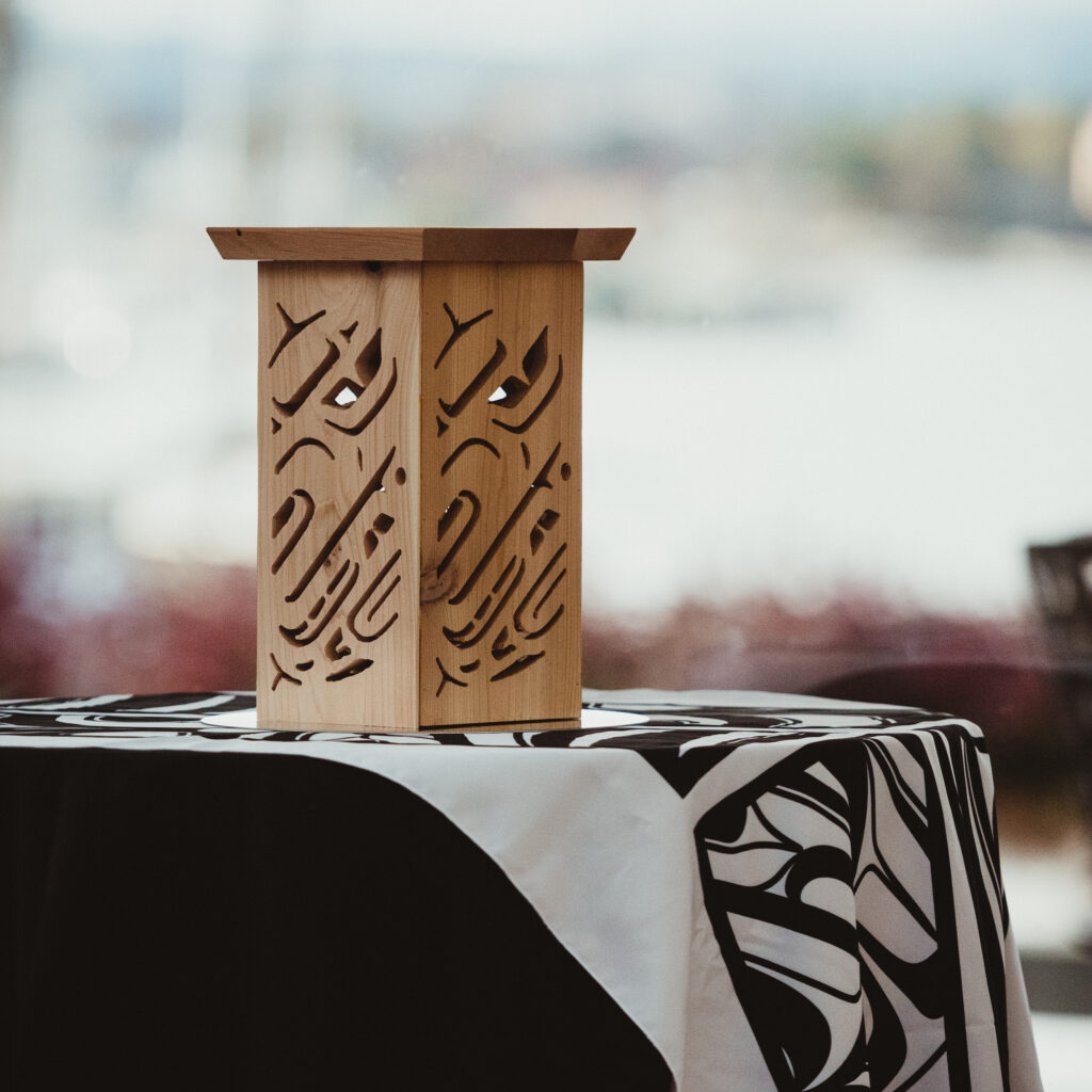 Wooden lantern with carved patterns sits on a table covered with a black and white patterned cloth.